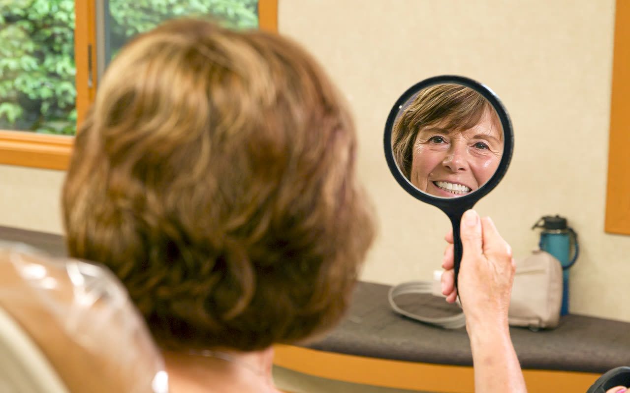 Orthodontic patient admiring her new smile in a hand mirror in Grand Rapids, MI