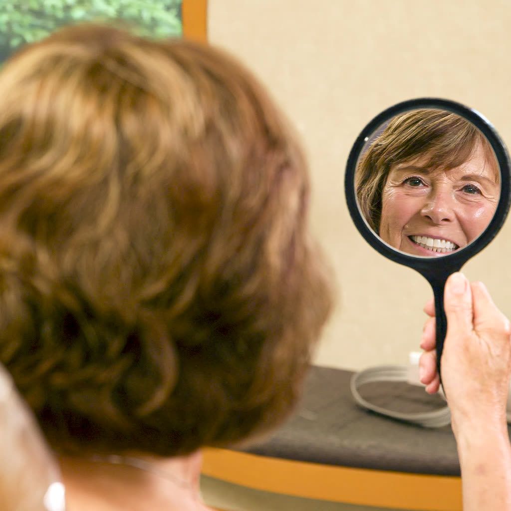 Orthodontic patient admiring her new smile in a hand mirror in Grandville, MI